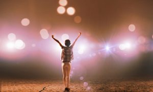 44908298 - back view of girl with hands up standing in stage lights